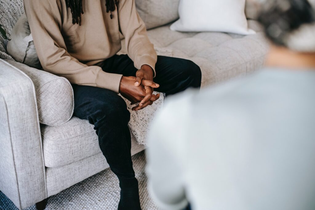 young black man sitting on sofa speaking to someone whose back is to the camera
